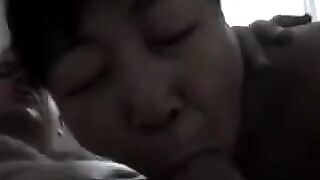 An adult Chinese woman practices her blowjob skills on her man in bed